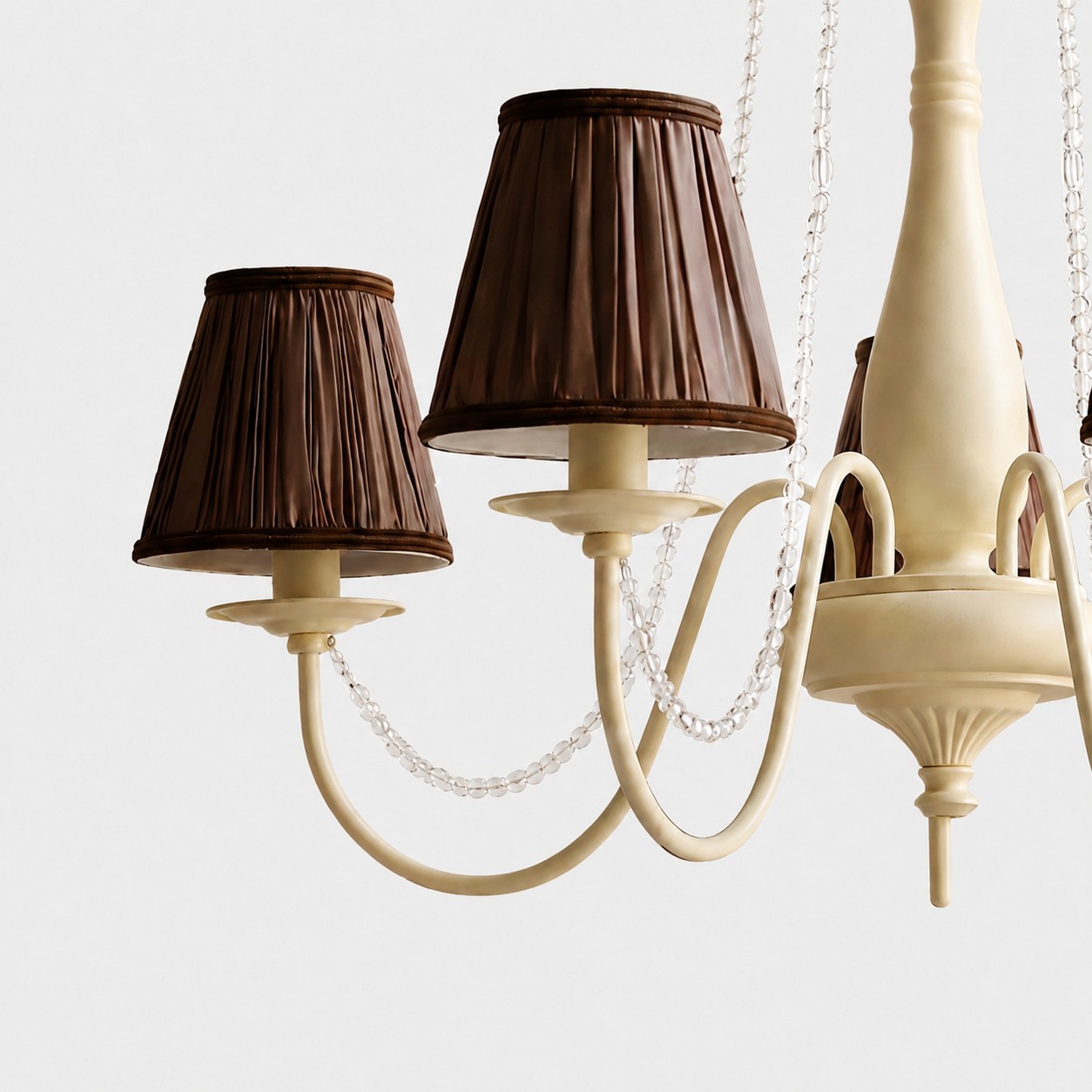 Close-up of cream iron chandelier body with curved arms and bead trim